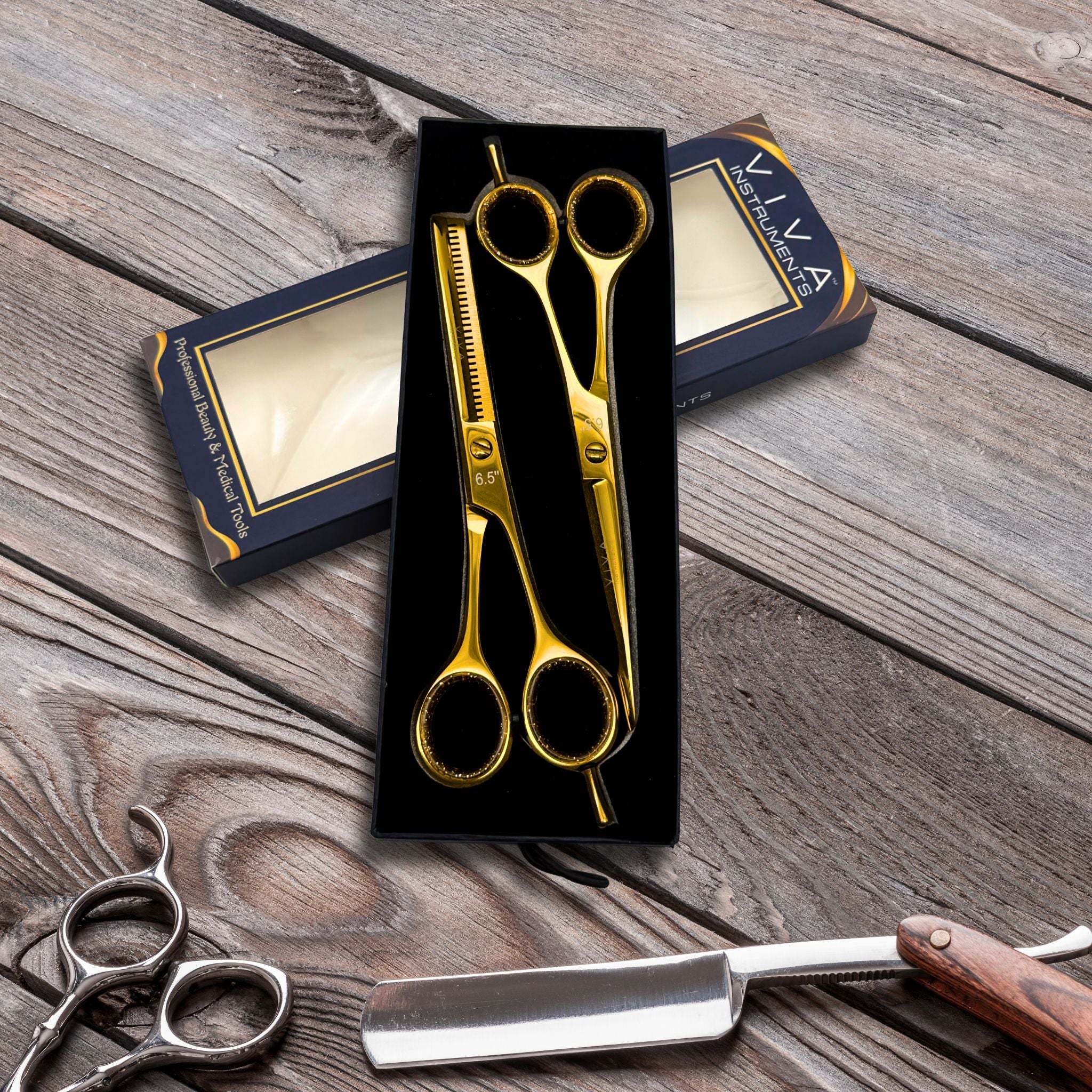 Gold scissors in a black box on a wooden surface with a razor and other tools.