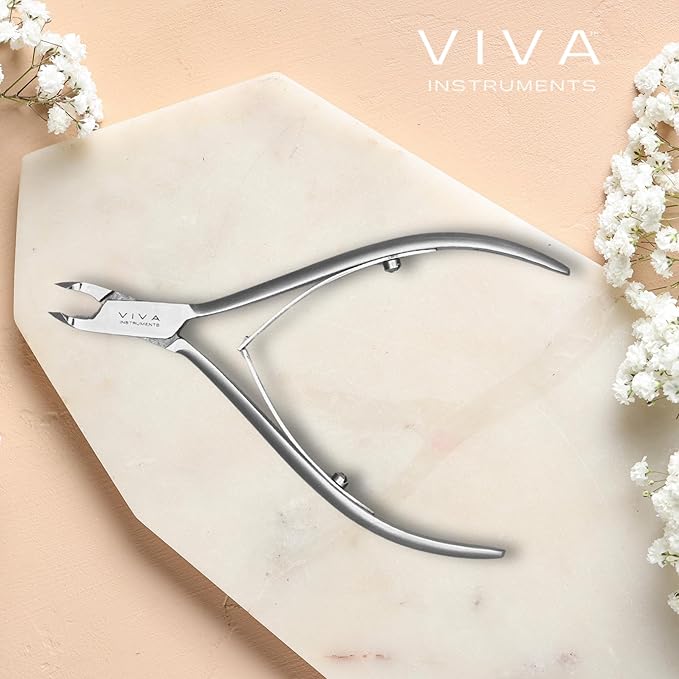 Cuticle Nail clippers with 'VIVA Instruments' branding on a marble surface with white flowers.