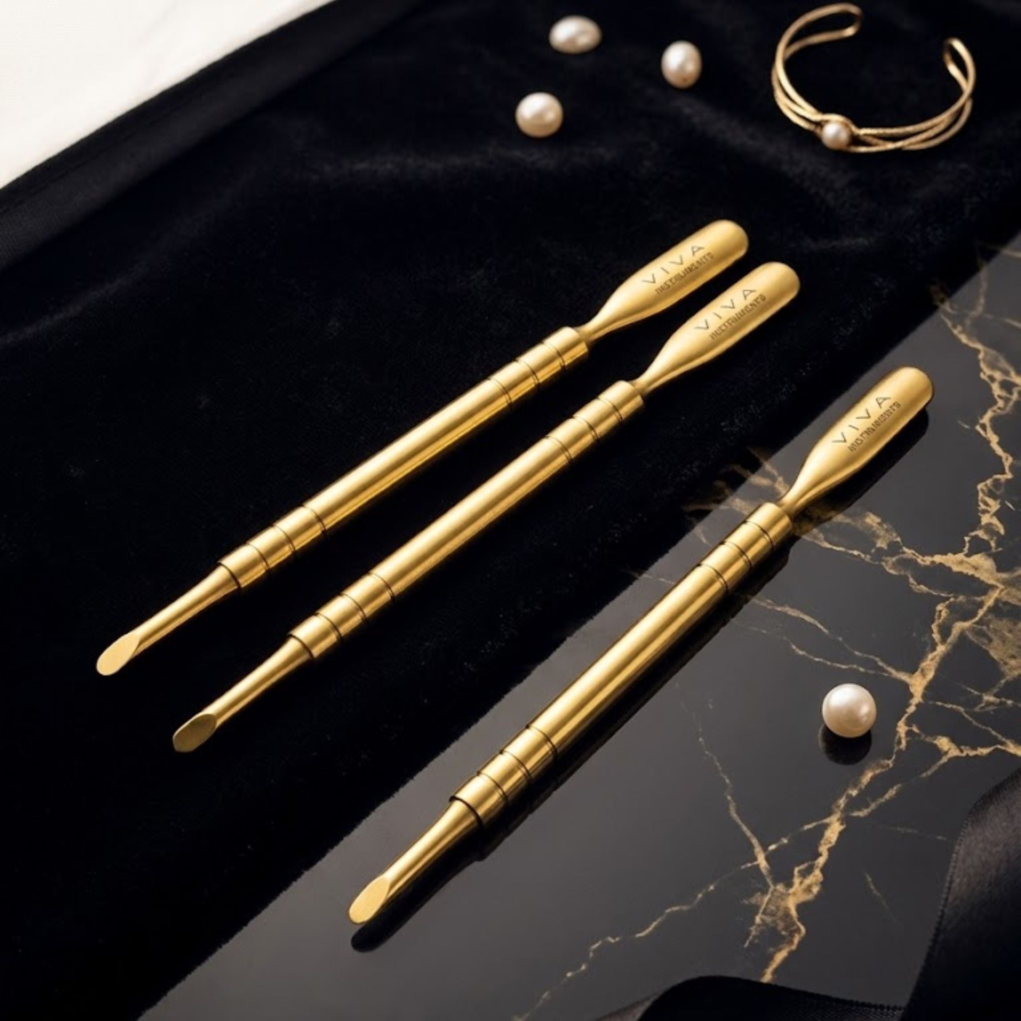 Gold cuticle pushers nail tools with 'VIVA' branding on a black and gold marble surface.