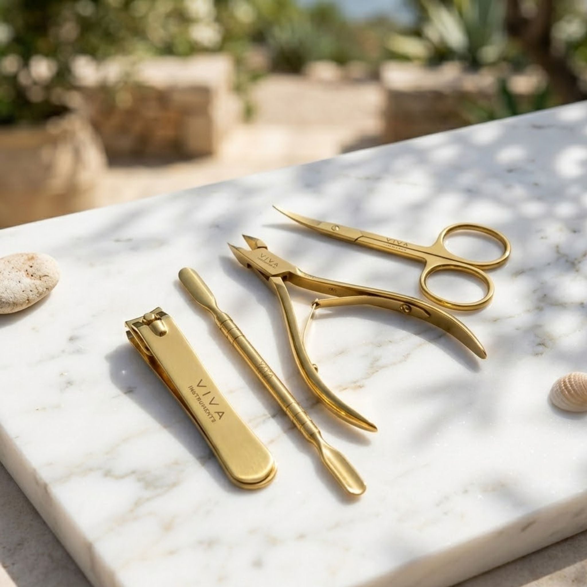 Gold nail care tools including a clipper, scissors, and cuticle nipper on a marble surface with a natural background. - viva instruments
