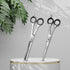 Set of two pairs of scissors on a white pedestal with a gray background and green leaves.
