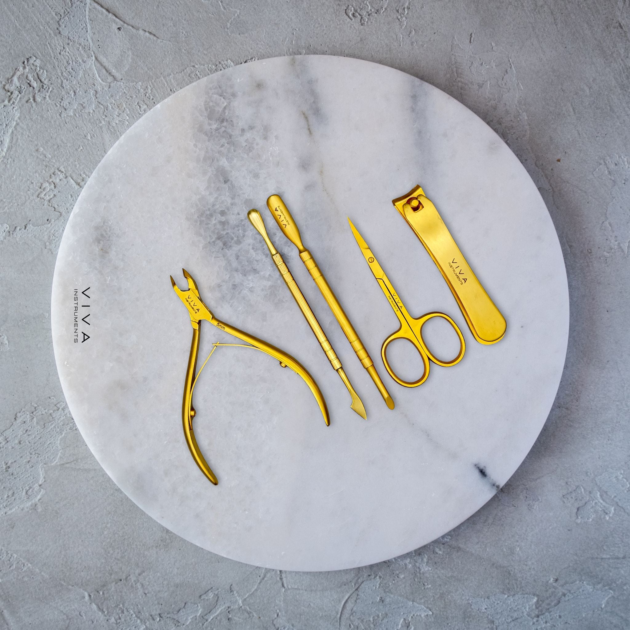 Set of gold nail care tools on a marble plate with 'VIVA' branding.